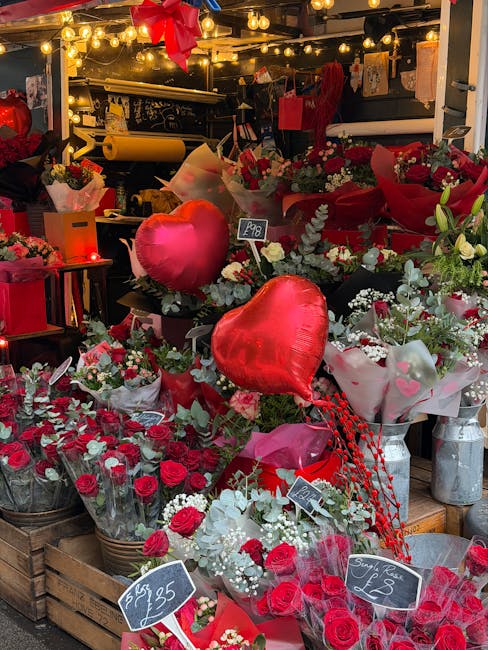 An abundant display of fresh floral arrangements and bouquets at a flower shop, featuring vibrant red roses, white baby's breath, and greenery, arranged in wicker baskets, plastic wraps, and vases. Th