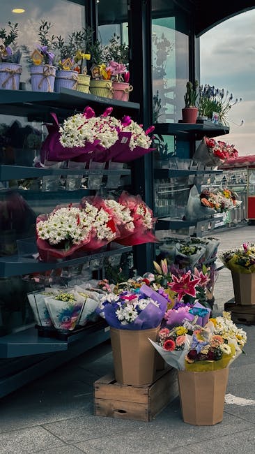 A display of fresh floral arrangements and bouquets outside a flower shop, featuring a variety of colorful flowers including white daisies, pink lilies, purple irises, and yellow tulips, all wrapped i
