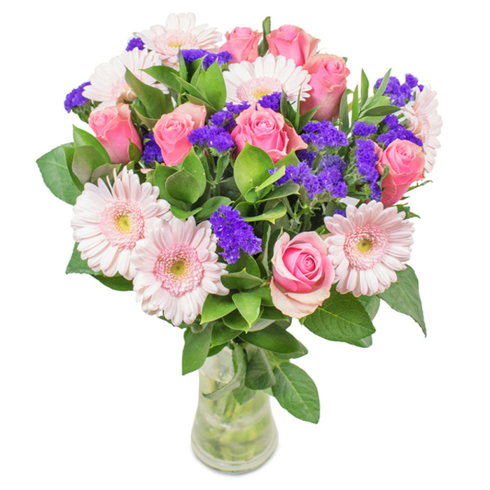 Set against a crisp, white background reminiscent of a sunlit Bracknell Forest morning, this vibrant floral bouquet stands proudly in a clear glass vase. At its heart, around seven to nine medium pink roses are grouped, their classic spiral curls suggesting both refinement and fresh blooming. These are complemented by five to seven pale pink Gerbera daisies, their large, round faces and pale, almost white centres recalling the delicate wildflowers scattered across South Hill Park. Throughout the bouquet, clusters of bright purple statice act as eye-catching accents, their papery texture and rich hue adding both contrast and lively movement, much like the unexpected pops of colour seen in local woodlands. Lush, deep green foliage provides a grounding base, amplifying the freshness and abundance symbolic of the forests and green spaces surrounding Bracknell. Each stem is visible through crystal-clear water, their alignment and vitality hinting at expert local floristry and the possibility of same-day freshness. Whether intended for birthdays, anniversaries, or as a daily splash of joy in home or office, this arrangement exudes the celebratory, affectionate spirit found throughout Bracknell Forest.